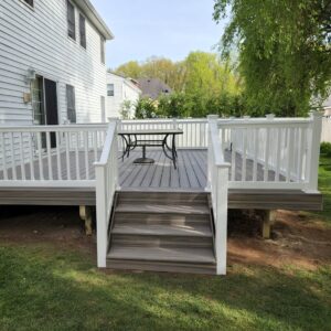Custom deck in Staten Island with gray composite decking, white railings, and central stair access.