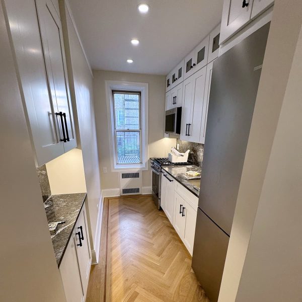 Custom galley kitchen renovation featuring white cabinetry, stainless steel appliances, dark countertops, and herringbone hardwood floors.