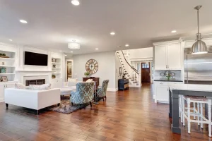 Open-concept living space with modern kitchen, hardwood floors, built-in shelving, fireplace, recessed lighting, and staircase leading to upper level.